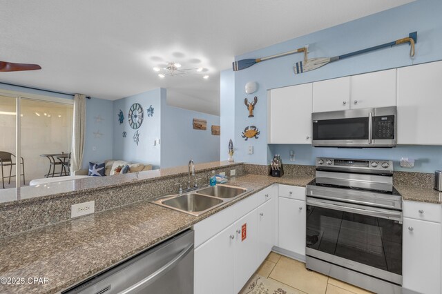 kitchen with light tile patterned floors, stainless steel appliances, open floor plan, white cabinets, and a sink