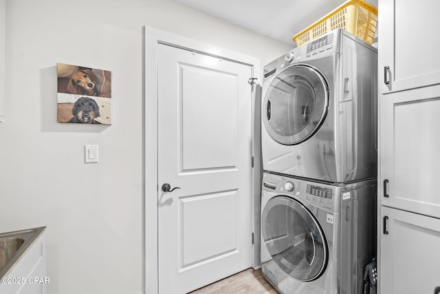 laundry area featuring cabinet space, light wood-type flooring, and stacked washer / dryer