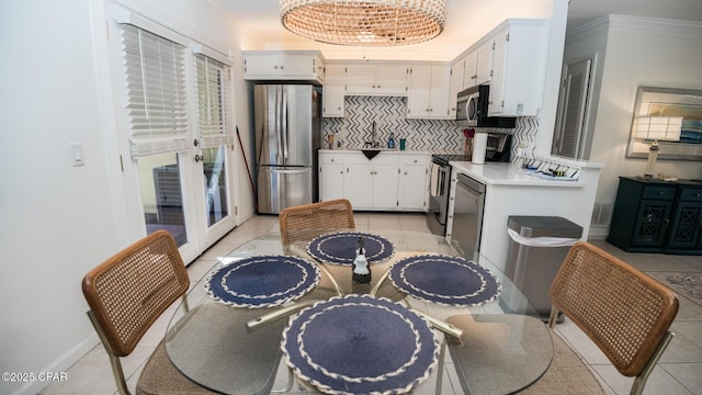 kitchen with appliances with stainless steel finishes, light countertops, ornamental molding, and white cabinetry