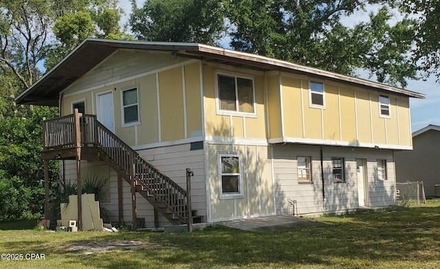 rear view of property featuring board and batten siding, a lawn, and stairs