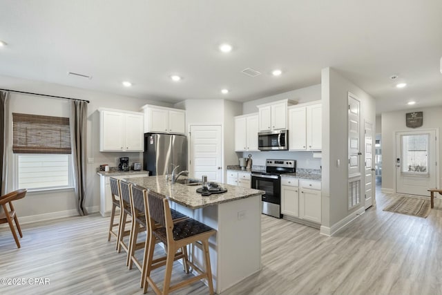 358 Sea Grove Way, Port St Joe, FL 32456 - kitchen with appliances with stainless steel finishes, light wood-type flooring, a center island with sink, a breakfast bar area, and white cabinetry