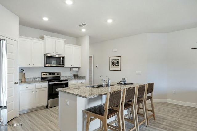 358 Sea Grove Way, Port St Joe, FL 32456 - kitchen with stainless steel appliances, light wood-style floors, light stone counters, a breakfast bar area, and white cabinetry