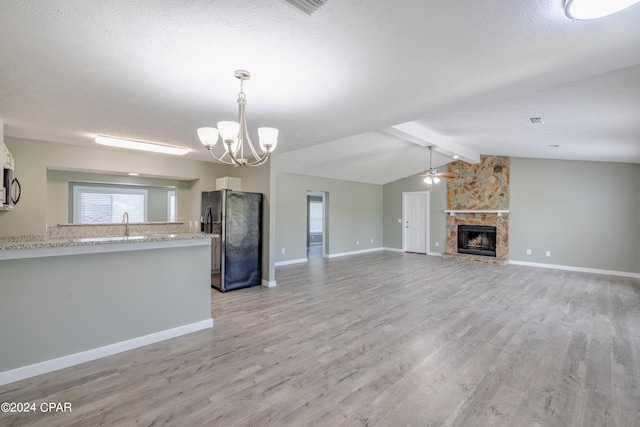 unfurnished living room with vaulted ceiling with beams, light wood-style flooring, ceiling fan with notable chandelier, and a stone fireplace