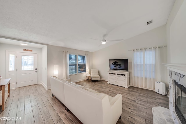 living room with wood finish floors, visible vents, a premium fireplace, a ceiling fan, and vaulted ceiling