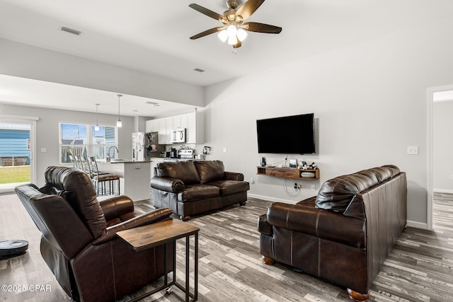 living room with light wood-style floors, ceiling fan, visible vents, and baseboards