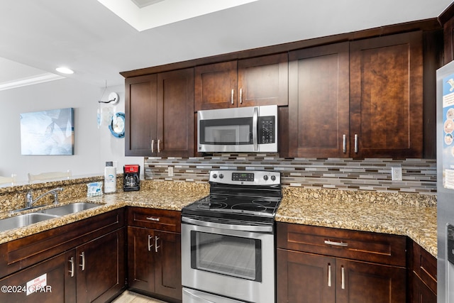 kitchen featuring stainless steel appliances, a sink, decorative backsplash, and light stone countertops