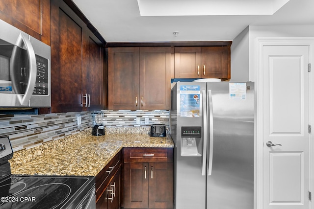 kitchen with dark brown cabinets, appliances with stainless steel finishes, decorative backsplash, and light stone counters