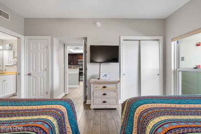 bedroom with ensuite bath, visible vents, and wood finished floors