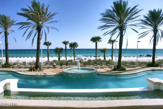 view of swimming pool featuring a community hot tub, a water view, and fence