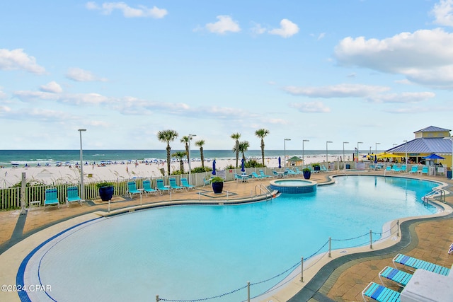 community pool featuring a patio area, fence, a hot tub, and a water view