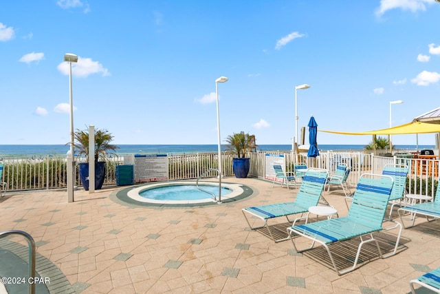 view of pool with a patio, a water view, fence, and a hot tub