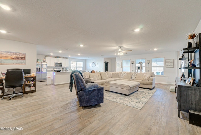 living room with a ceiling fan, a textured ceiling, light wood-style floors, and a healthy amount of sunlight