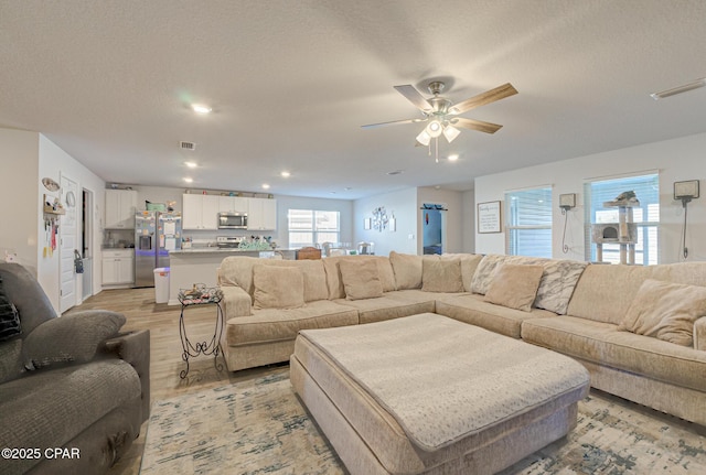 living area featuring visible vents, light wood-style floors, a ceiling fan, and a textured ceiling