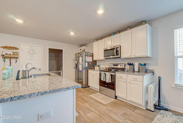 kitchen with a sink, light wood-style flooring, appliances with stainless steel finishes, and white cabinets