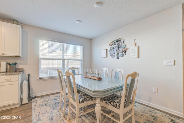 dining room featuring light wood-style floors, baseboards, and a textured ceiling