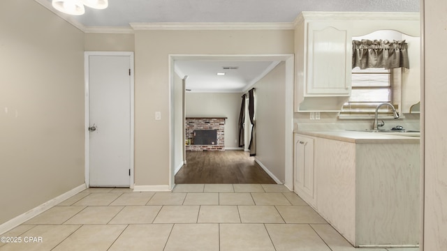 hall featuring ornamental molding, baseboards, a sink, light tile patterned flooring, and visible vents