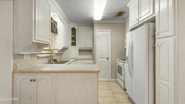 kitchen featuring light tile patterned flooring, a textured ceiling, a peninsula, white appliances, and a sink