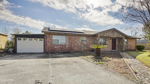 single story home with solar panels, an attached garage, brick siding, and driveway