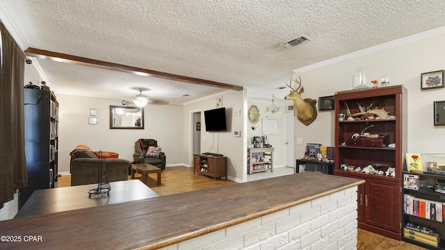 interior space featuring visible vents, ornamental molding, a textured ceiling, wood finished floors, and baseboards