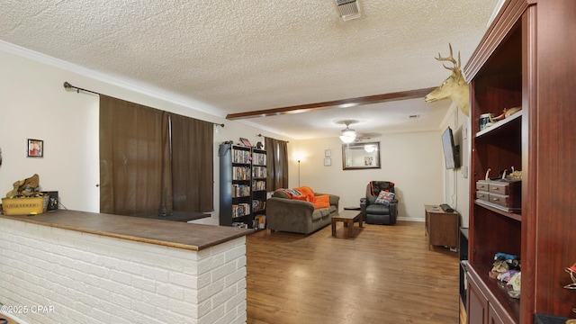 living room with baseboards, a textured ceiling, visible vents, and wood finished floors