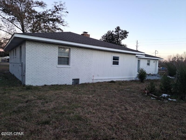 view of home's exterior with brick siding, a lawn, a chimney, and fence