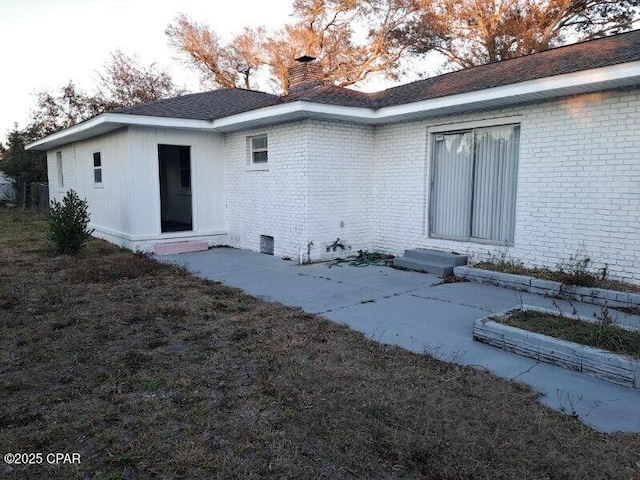 back of house with entry steps, a chimney, and brick siding