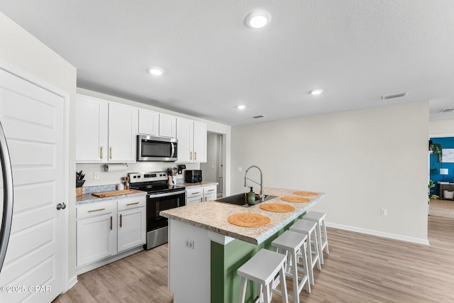 kitchen featuring a kitchen island with sink, stainless steel appliances, a sink, light wood-style floors, and a kitchen breakfast bar