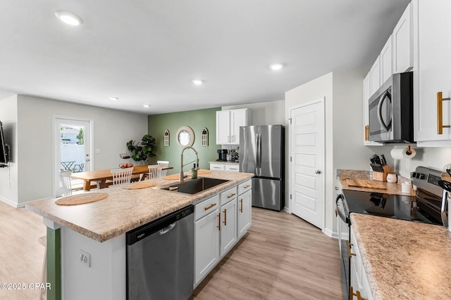 kitchen featuring stainless steel appliances, an island with sink, a sink, and light wood-style flooring