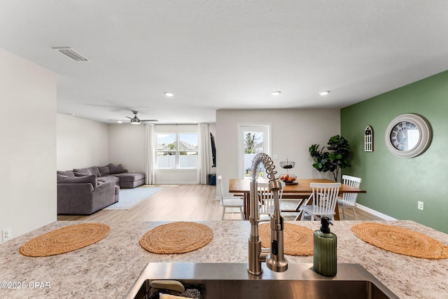 interior space with visible vents, a ceiling fan, a sink, wood finished floors, and baseboards