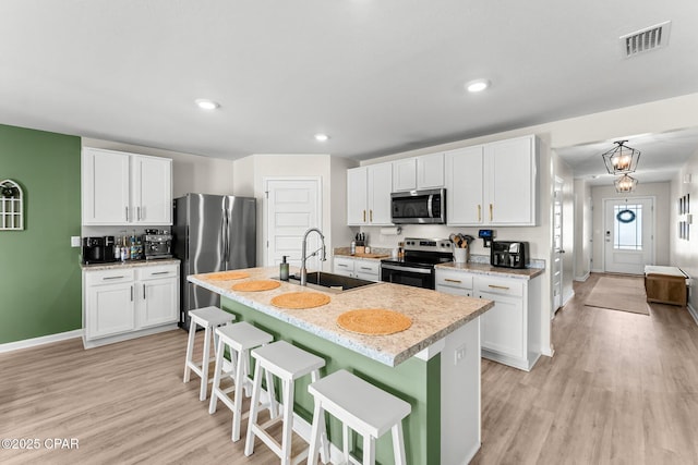 kitchen with light wood-style flooring, stainless steel appliances, a breakfast bar, a sink, and visible vents