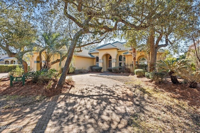 mediterranean / spanish-style home with decorative driveway, a tile roof, and stucco siding