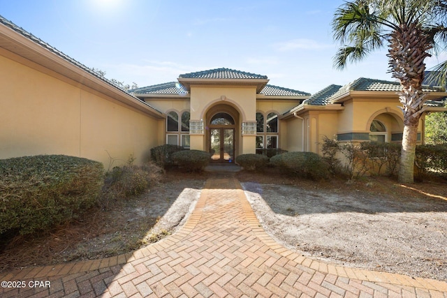 view of exterior entry with french doors, a tile roof, and stucco siding