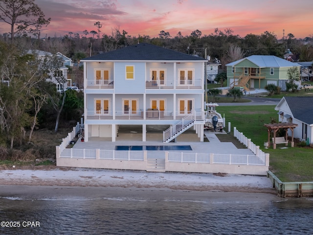 back of house at dusk with a balcony, a patio area, a fenced backyard, and french doors