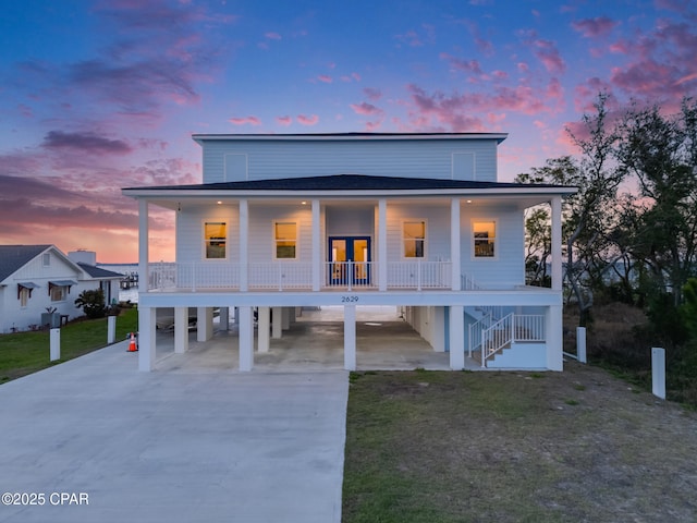 beach home with a porch, concrete driveway, a carport, and stairs