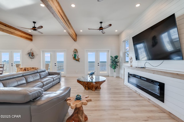 living room with a wealth of natural light, a glass covered fireplace, french doors, and beam ceiling