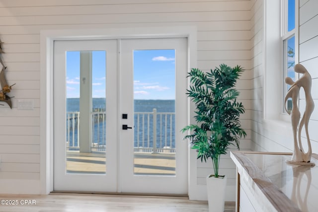 doorway with light wood finished floors, wood walls, and plenty of natural light