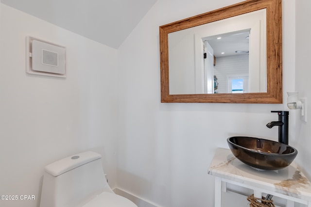 half bath with lofted ceiling, a sink, and toilet