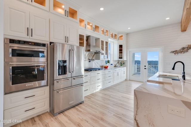 kitchen featuring stainless steel appliances, a sink, french doors, light stone countertops, and wall chimney exhaust hood