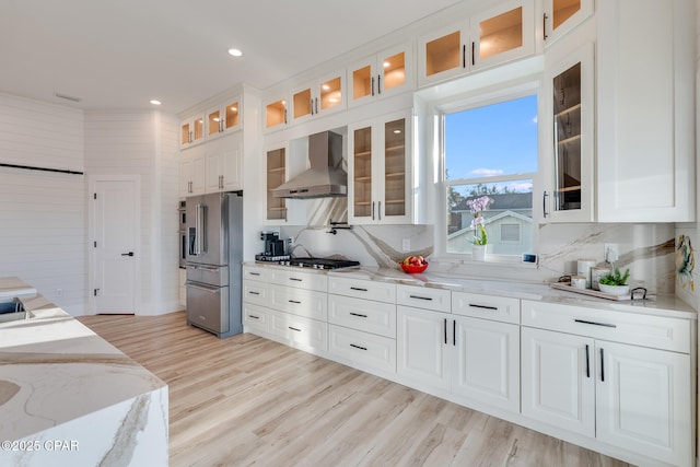 kitchen with backsplash, light wood-style floors, white cabinets, wall chimney range hood, and high end refrigerator