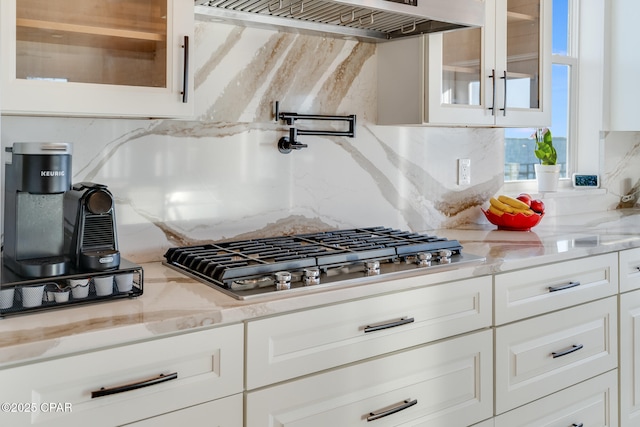 kitchen with stainless steel gas cooktop, extractor fan, glass insert cabinets, and light stone countertops