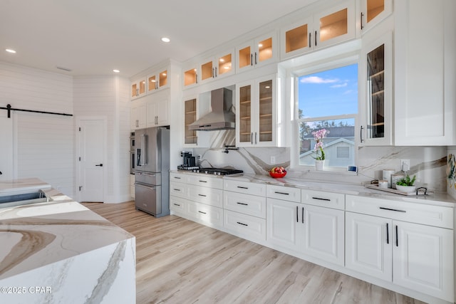 kitchen with stainless steel appliances, white cabinets, wall chimney exhaust hood, and a barn door