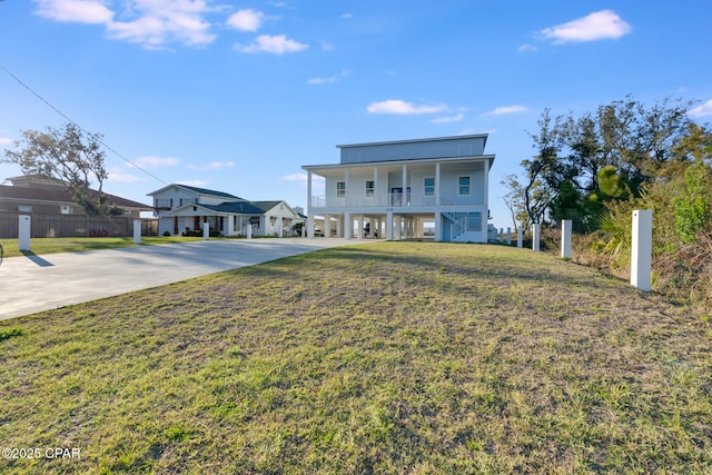 coastal home featuring concrete driveway, a balcony, a front lawn, and stairs