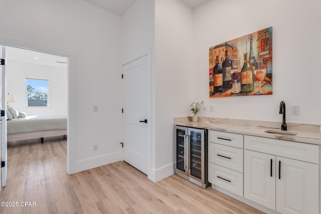 bar with light wood finished floors, beverage cooler, baseboards, indoor bar, and a sink