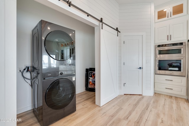 laundry area with stacked washer and dryer, a barn door, laundry area, and light wood-style floors