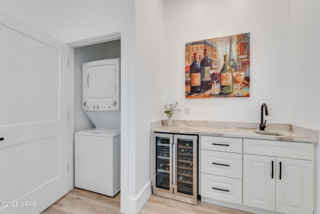 laundry area featuring stacked washer and dryer, laundry area, light wood-style flooring, wine cooler, and indoor wet bar