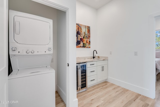 laundry room featuring beverage cooler, laundry area, a sink, light wood-type flooring, and stacked washing maching and dryer