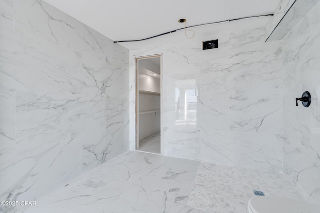 full bathroom with marble finish floor, toilet, a marble finish shower, and stone wall