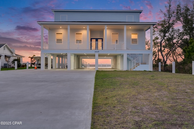 coastal inspired home featuring a porch, concrete driveway, a lawn, a carport, and stairs