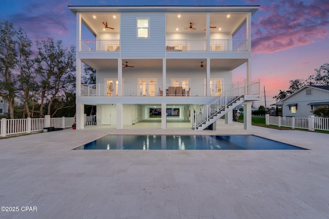 back of property at dusk featuring a ceiling fan, a patio, a balcony, stairs, and fence