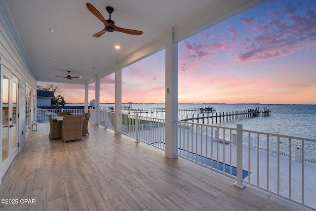 wooden deck with a dock, a water view, and ceiling fan